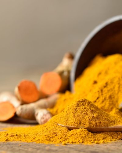 Close-up of Turmeric (curcumin) powder in  wooden spoon with bowl and fresh rhizome slices on wood background.